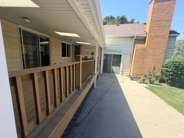 Covered outdoor patio with wood railing, multiple sliding glass doors, and a concrete pathway leading right in to a the family room.