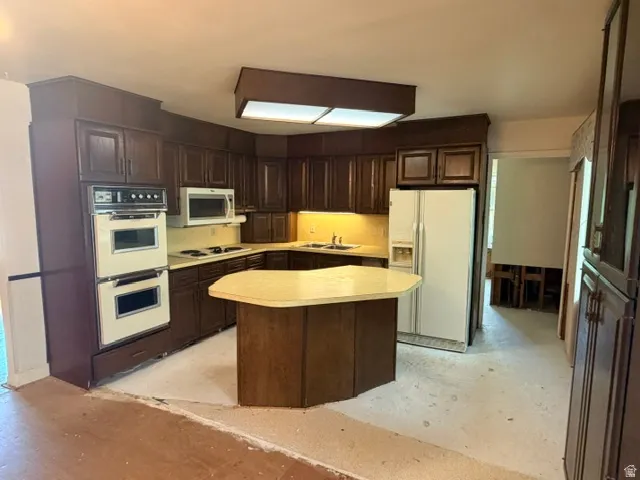 Spacious kitchen featuring dark wood cabinetry, a light-colored countertop, built-in double ovens, and an island with a complementary countertop.