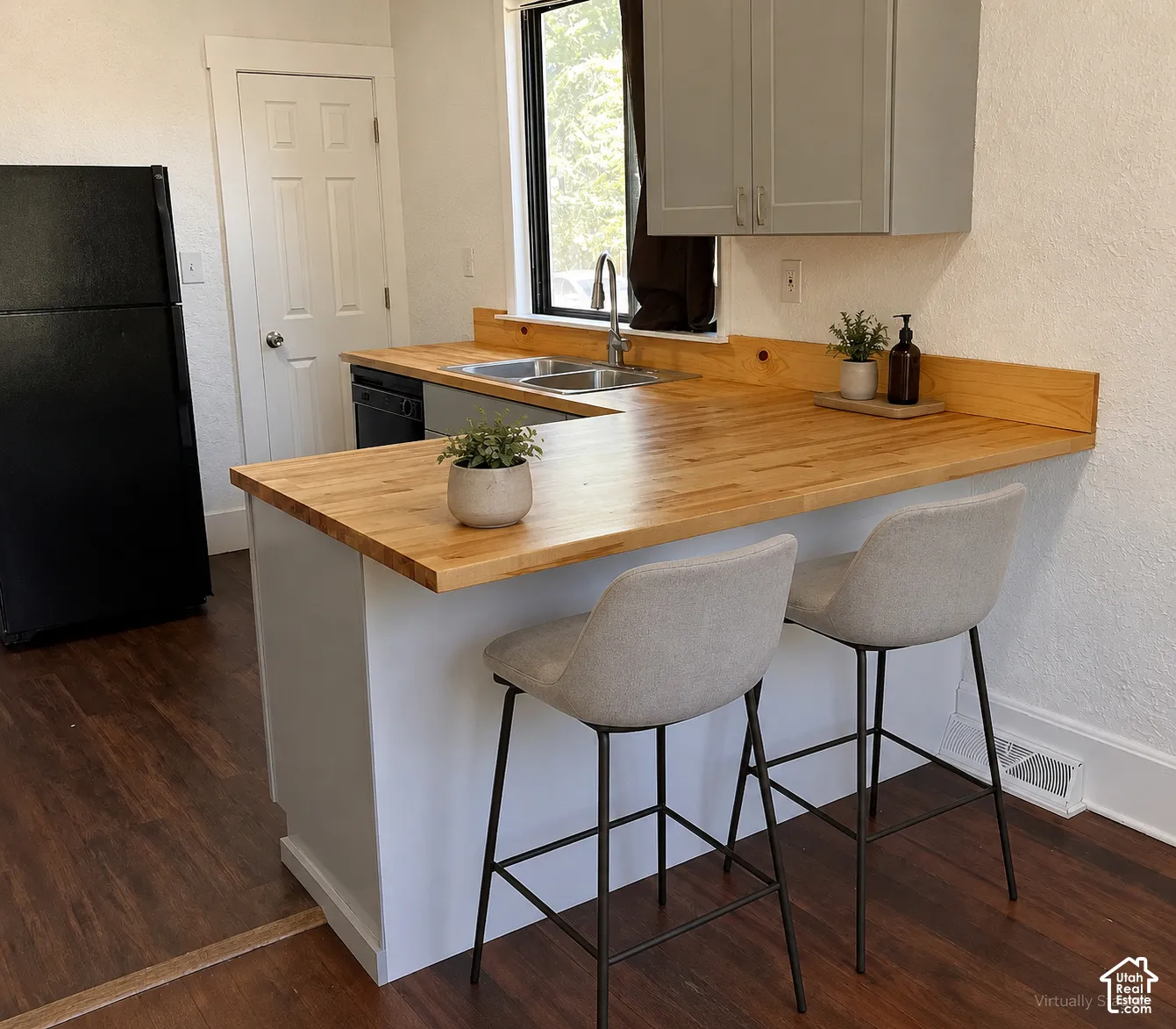 (Front Unit) Laminate wood-finish flooring, butcher block countertops, gray upper cabinetry, stainless steel double basin sink, and black appliances