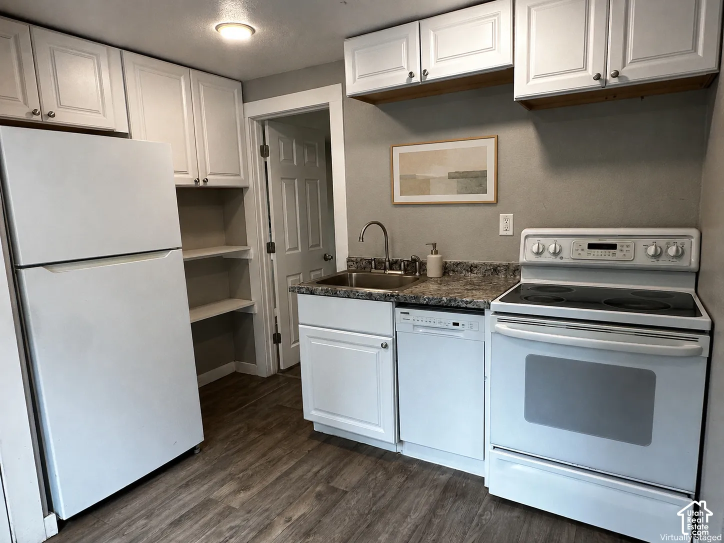 Kitchen featuring white cabinetry, wood-finish flooring, a stainless steel sink, and white appliances