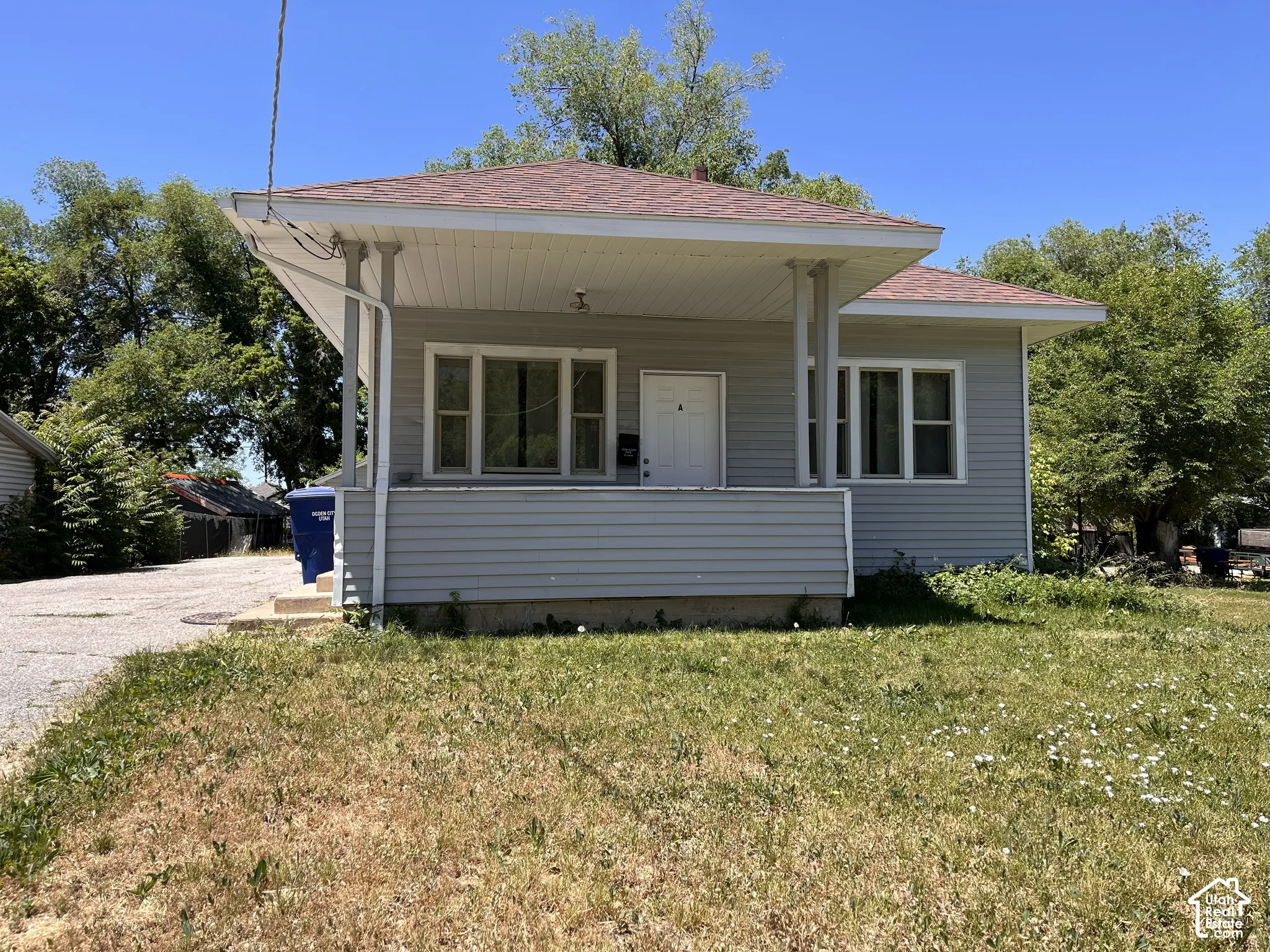 Single-story residence featuring light gray siding, a covered front porch, and a gravel driveway