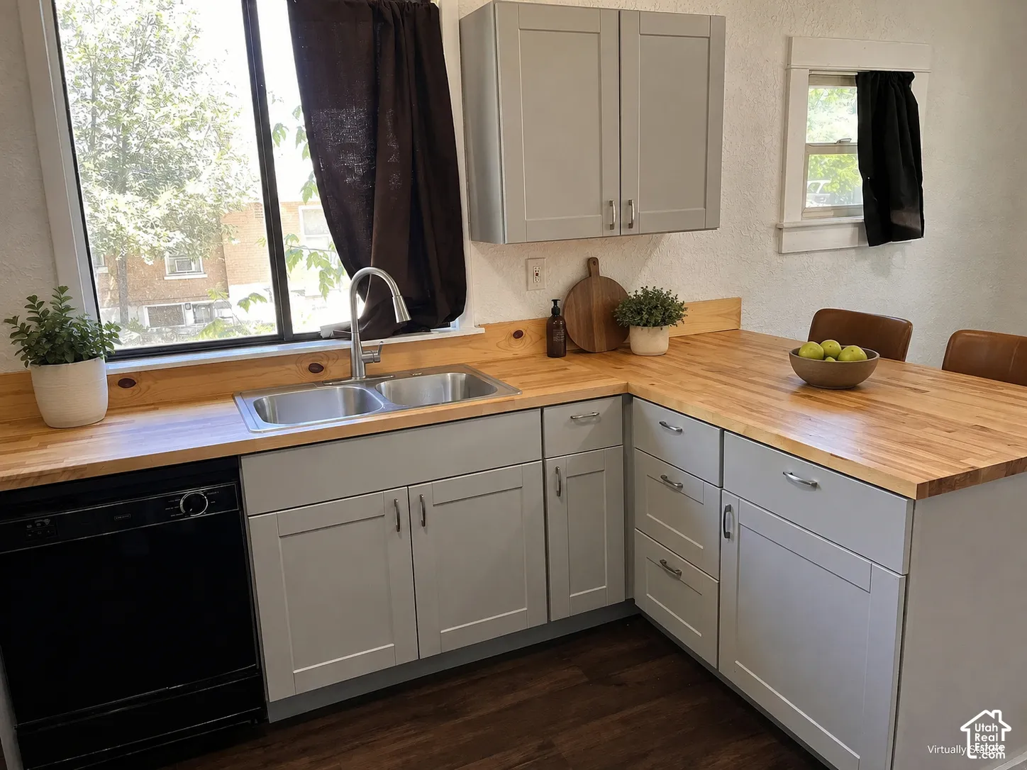 (Front Unit) Light gray cabinetry with brushed nickel hardware, butcher block countertops, dual basin stainless steel sink, black built-in dishwasher, and wood-finish flooring