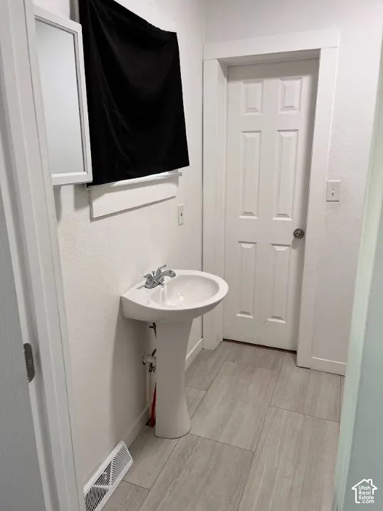 (Front Unit) Pedestal sink with chrome fixtures, wood-finish flooring, white paneled door, and a wall-mounted mirror