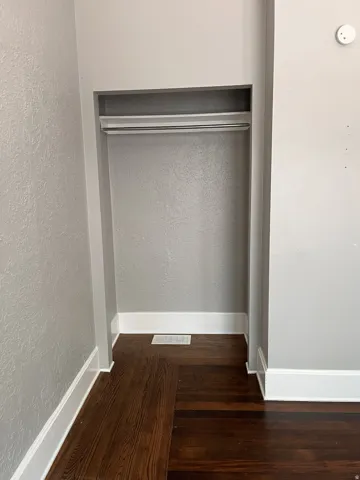 Built-in closet featuring a hanging rod and upper shelf, dark wood-finish flooring, and white trim