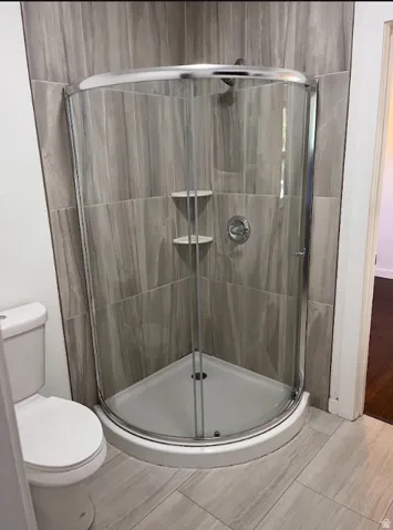 Corner shower enclosure with clear glass panels, chrome hardware, and integrated shelving