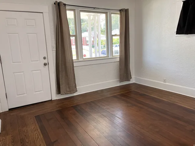 Rich wood-finish flooring, white paneled door, and bright window with white trim