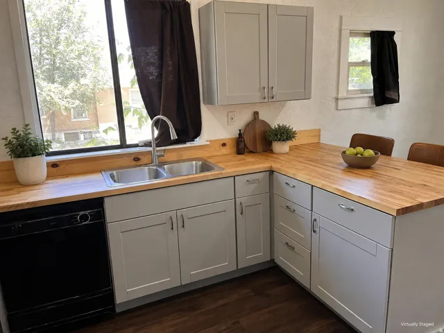 Light gray cabinetry with brushed nickel hardware, butcher block countertops, dual basin stainless steel sink, black built-in dishwasher, and wood-finish flooring