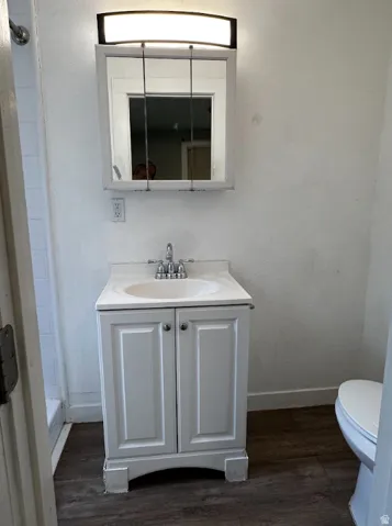 White vanity with a built-in sink, chrome fixtures, and wood-finish flooring