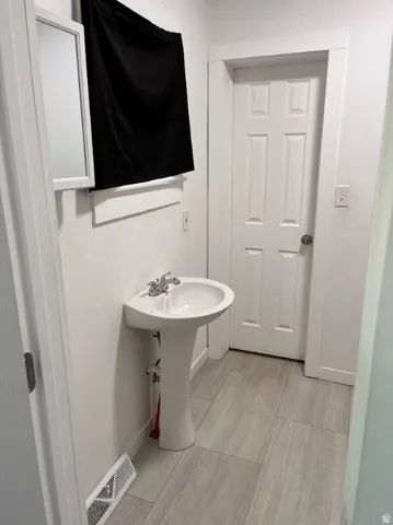 Pedestal sink with chrome fixtures, wood-finish flooring, white paneled door, and a wall-mounted mirror