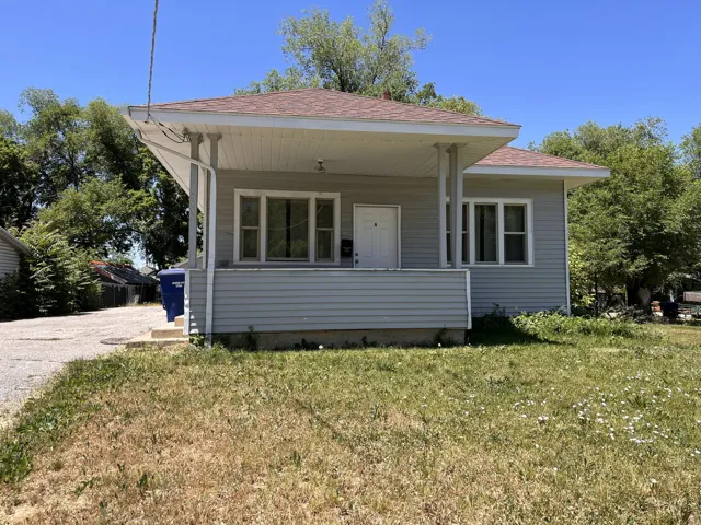 Single-story residence featuring light gray siding, a covered front porch, and a gravel driveway