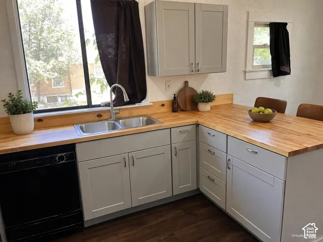 (Front Unit) Light gray cabinetry with brushed nickel hardware, butcher block countertops, dual basin stainless steel sink, black built-in dishwasher, and wood-finish flooring