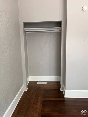 (Front Unit) Built-in closet featuring a hanging rod and upper shelf, dark wood-finish flooring, and white trim