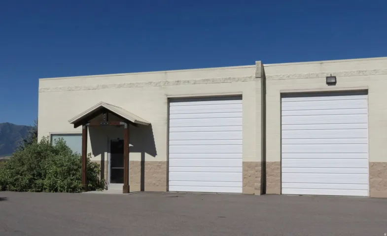 Two white roll-up garage doors, a covered entry with wood posts, and a window on a light-colored stucco exterior