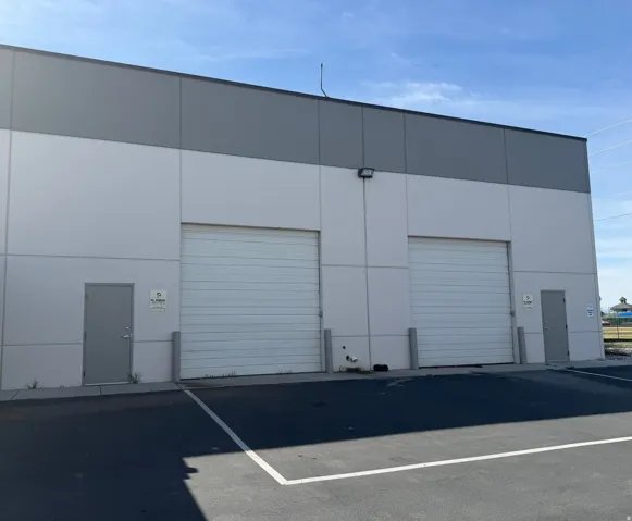 Building exterior with two roll-up doors, two pedestrian entry doors, and a paved parking area