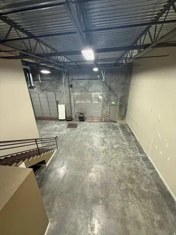 Exposed structural ceiling with fluorescent lighting, concrete flooring, and metal railing staircase
