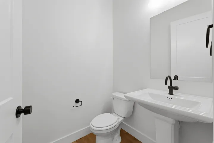 Pedestal sink with black-finish faucet, framed mirror, and wood-finish flooring