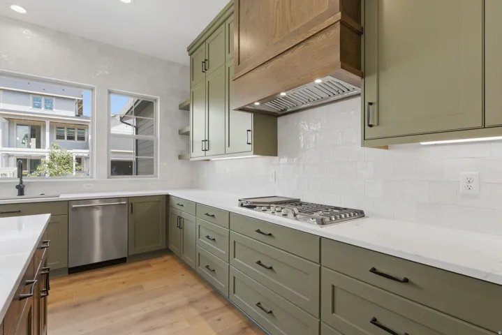 Kitchen featuring light green cabinetry, white countertops, wood-finish flooring, a stainless steel dishwasher, and a gas range with a built-in hood