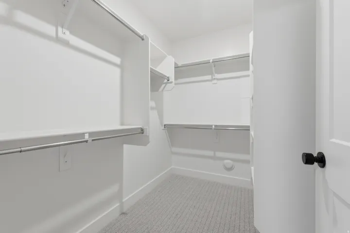 Walk-in closet with white shelving, multiple hanging rods, and light gray carpet