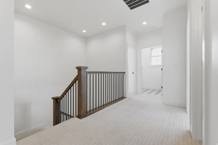 Bright upper-level hallway featuring light wood-finish flooring, recessed ceiling lighting, and a custom wood stair railing with metal balusters