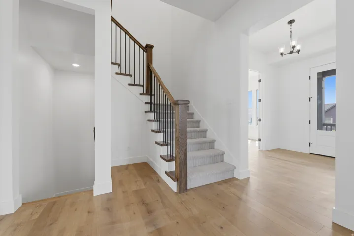 Hardwood-finish flooring, staircase with wood handrail, metal balusters, and carpeted treads, recessed lighting, and a chandelier with glass shades