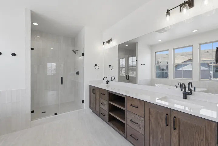 Primary suite. Dual vanity with white countertops, dark wood-finish cabinetry, and matte black fixtures