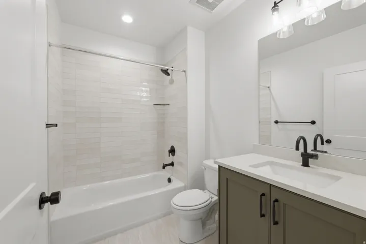 Spa-inspired bathroom featuring a frameless glass-enclosed shower with subway tile surround, soaking tub, white quartz countertop, dual-sink vanity with olive-finish cabinetry, matte black hardware and faucetry, and recessed ceiling lighting