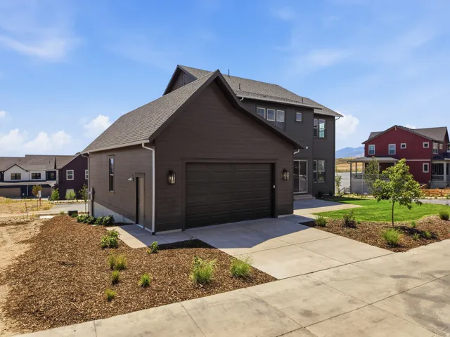 Dark-toned siding exterior with an attached garage, paved driveway, and landscaping featuring wood chips and newly planted greenery