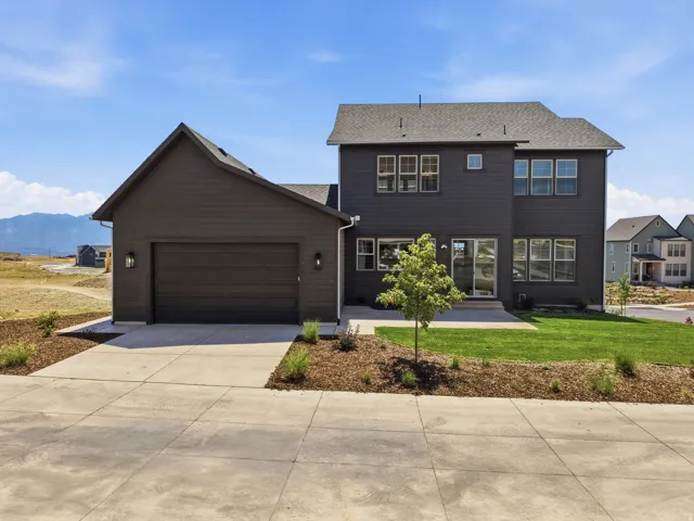 Two-story exterior with dark horizontal siding, an attached garage, a concrete driveway, and a backyard featuring a lawn and patio