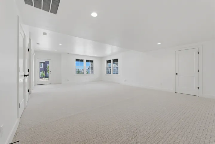 Spacious room featuring light-toned carpeting, multiple windows, recessed lighting, and white paneled doors