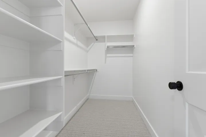 Walk-in closet featuring built-in shelving, multiple hanging rods, and light-toned carpeting