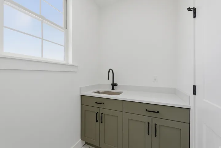 Utility sink with a matte black faucet, light-toned countertop, and sage green cabinetry