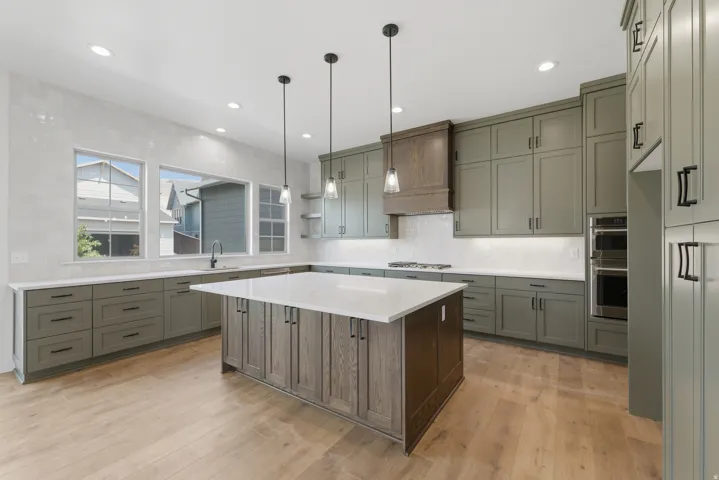 Kitchen featuring an expansive island with a white countertop, wood-finish flooring, custom cabinetry, stainless steel double ovens, and a gas range