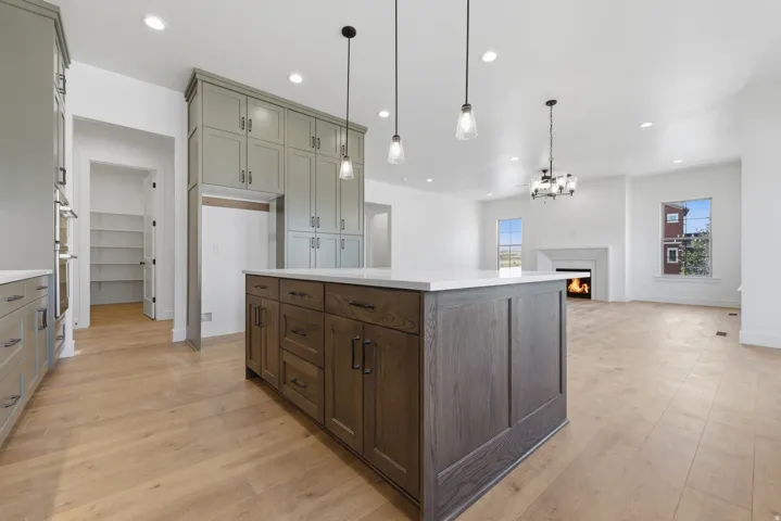 Spacious kitchen featuring an expansive center island with a light-toned countertop, extensive built-in cabinetry, wood-finish flooring, and recessed lighting