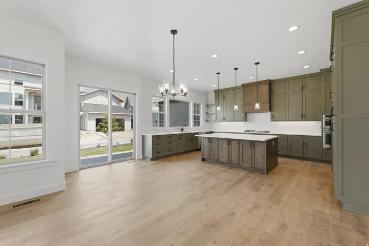 Open-concept kitchen featuring olive green cabinetry, wood-finish flooring, a large kitchen island with integrated storage, and a built-in wall oven
