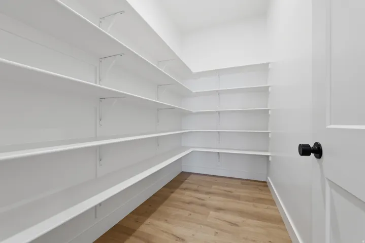 Expansive pantry with extensive white shelving, wood-finish flooring, and a white paneled door with a matte black knob