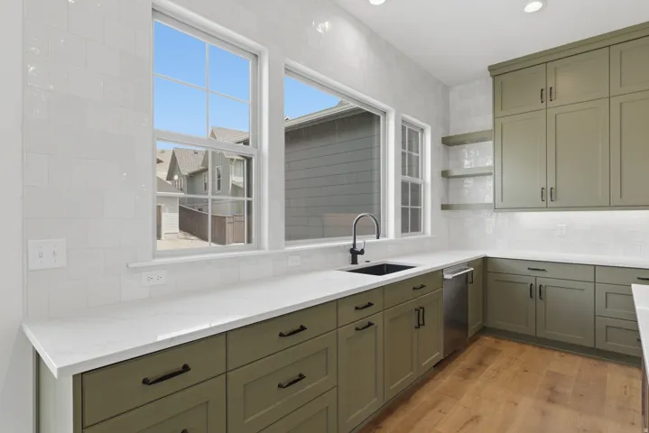 Kitchen featuring wood-finish flooring, white countertops, green cabinetry, a black sink, and a black faucet