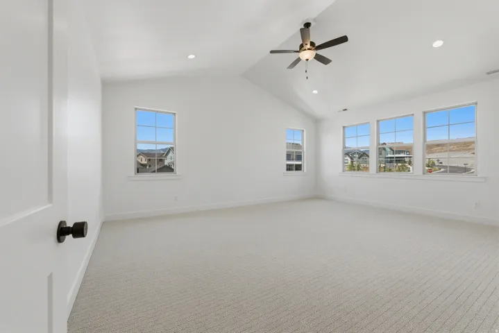 Primary suite. Vaulted ceiling with a ceiling fan, recessed lighting, multiple windows, and light-toned carpet