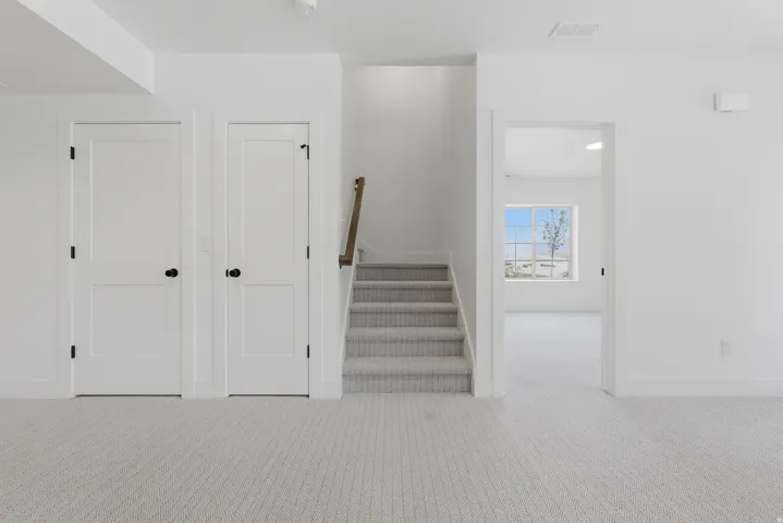 White interior doors with black hardware, light-toned carpet flooring, white walls, and a staircase with a wood-finish handrail