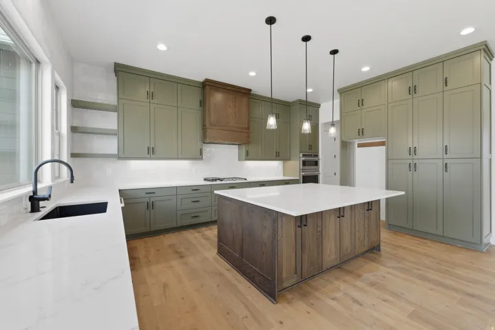 Kitchen featuring olive-toned cabinetry, light wood-finish flooring, a central island with a light countertop, a built-in cooktop, and pendant lighting
