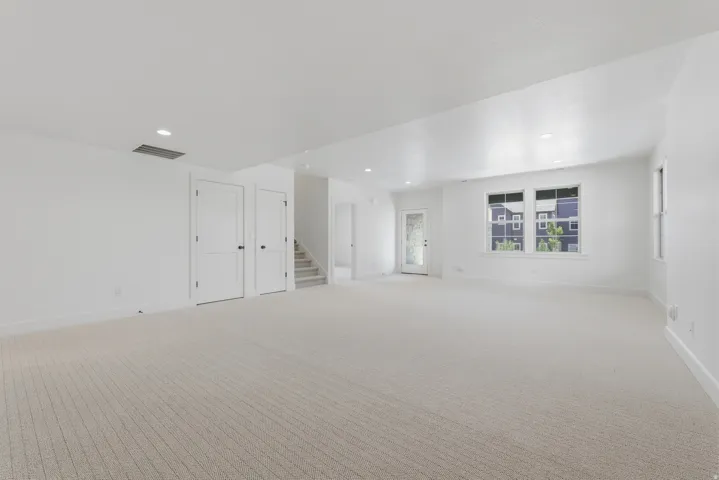 Spacious open-concept room featuring pristine wall-to-wall carpeting, recessed ceiling lighting, and multiple white panel doors providing access to adjoining spaces
