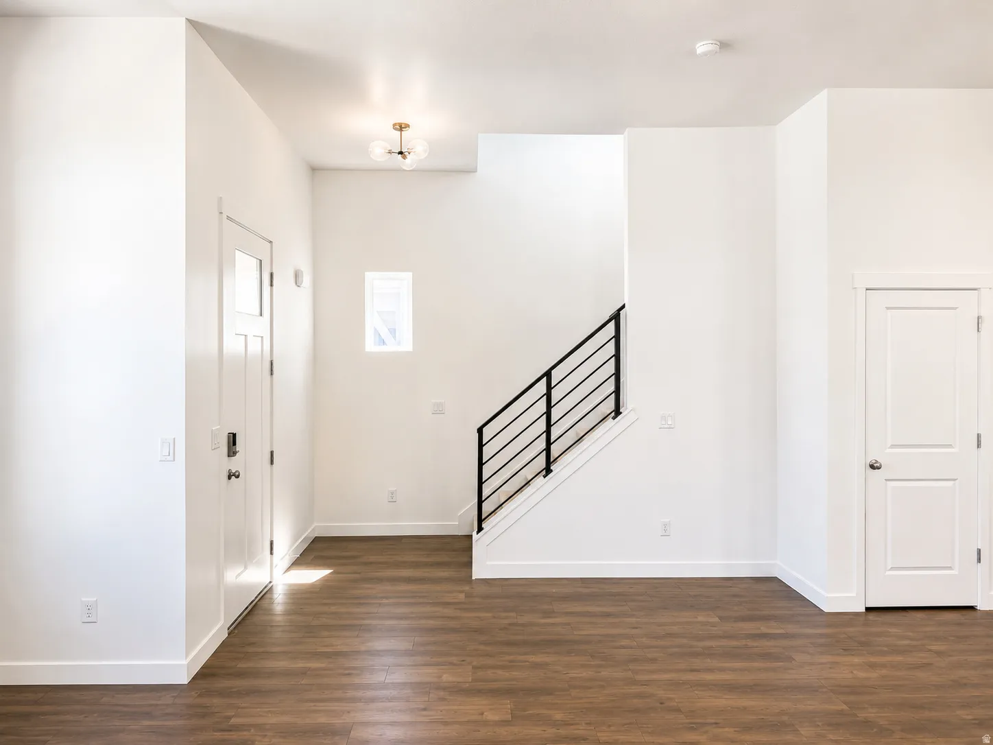 Wood-finish flooring, white paneled doors, modern black metal stair railing, and a contemporary ceiling light fixture