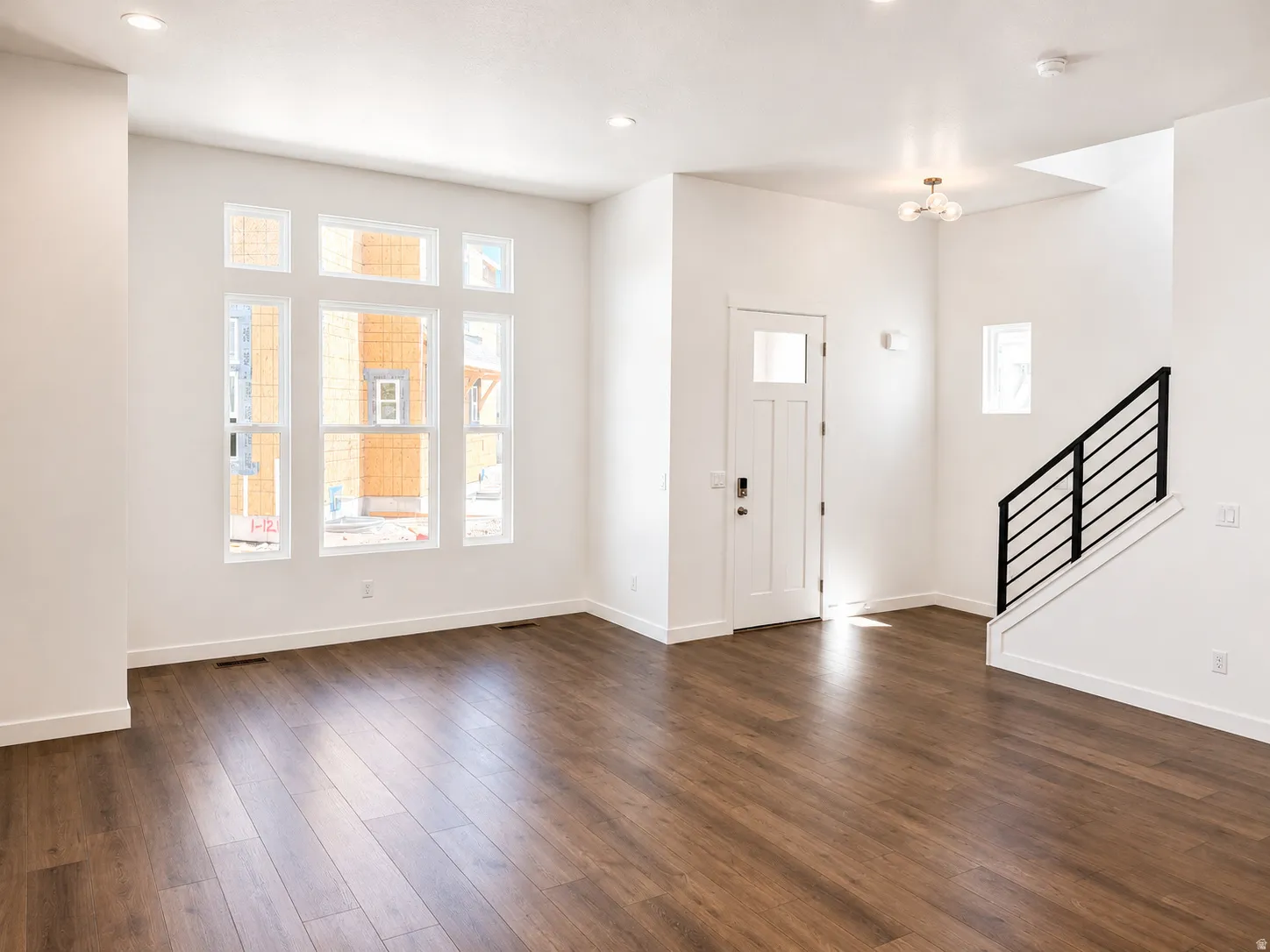 Wood-finish flooring, recessed lighting, white walls, large multi-pane windows, and a modern staircase with black railings