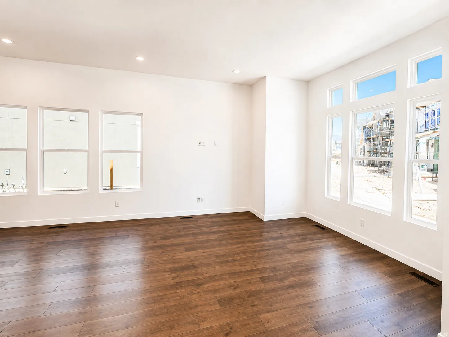 Expansive room featuring wood-finish flooring, white walls, recessed ceiling lighting, and multiple large windows