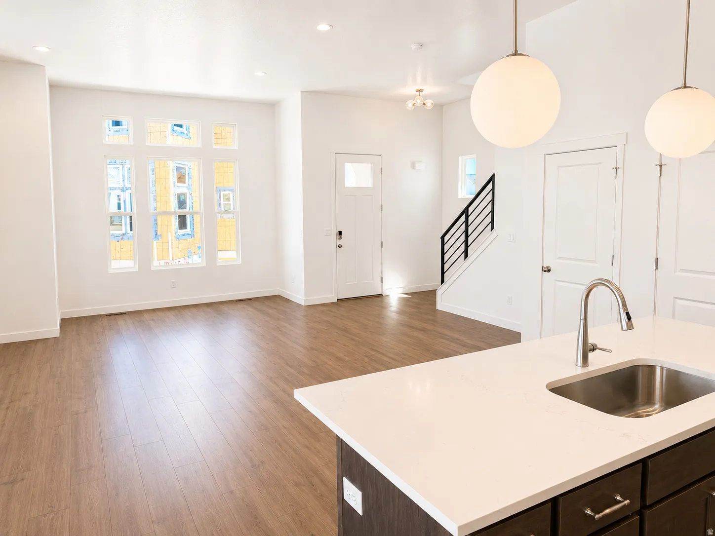 Open-concept living space featuring wood-finish flooring, recessed lighting, and a prominent kitchen island with a stainless steel sink and gooseneck faucet