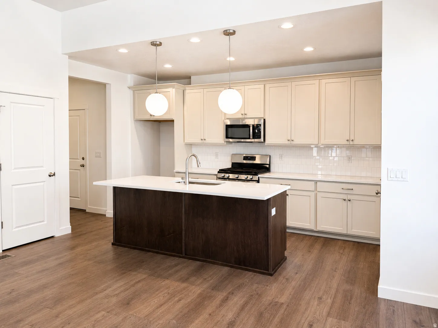 Kitchen featuring wood-finish flooring, a central island with a white countertop, two pendant lights, recessed lighting, and stainless steel appliances