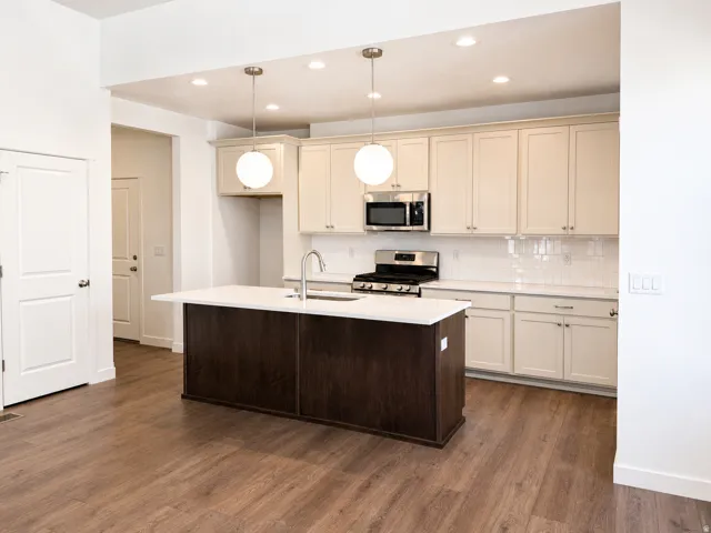Kitchen featuring wood-finish flooring, a central island with a white countertop, two pendant lights, recessed lighting, and stainless steel appliances