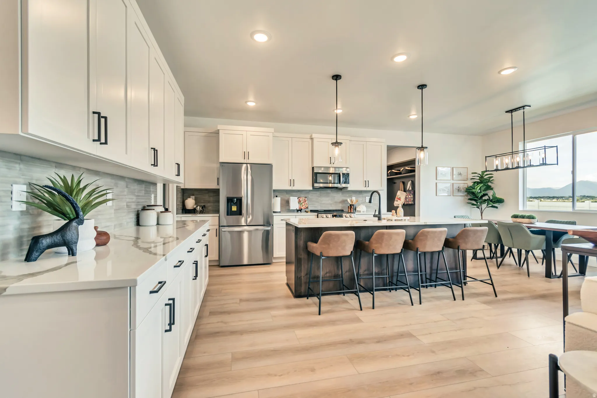 Bright kitchen featuring white cabinetry, stainless steel appliances, a center island with pendant lighting, and wood-finish flooring