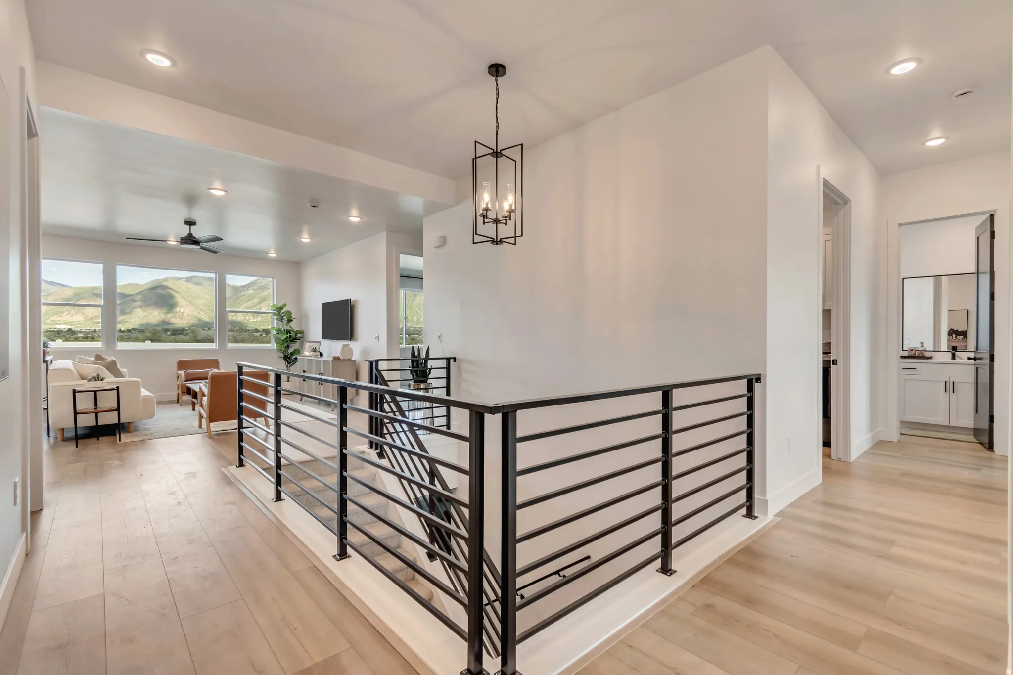 Light wood-finish flooring throughout, modern black metal stair railing, recessed lighting, and a contemporary black chandelier