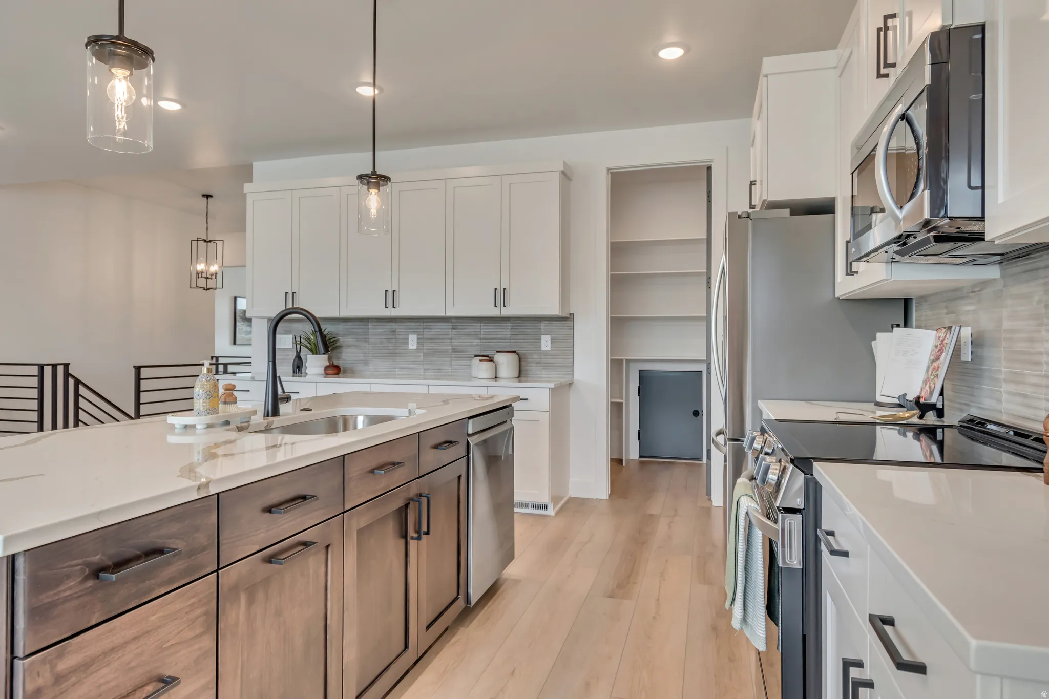 Modern kitchen with wood-finish flooring, a white countertop island featuring an undermount sink, and stainless steel appliances