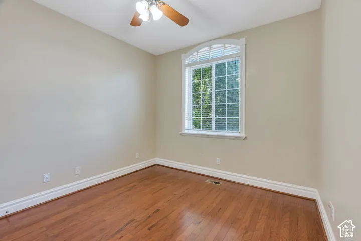 Hardwood flooring, arched window with grilles, integrated ceiling fan with lighting, and neutral wall paint